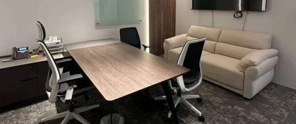 Spacious office with a large desk, meeting chairs, sofa, and wall-mounted TV for presentations.